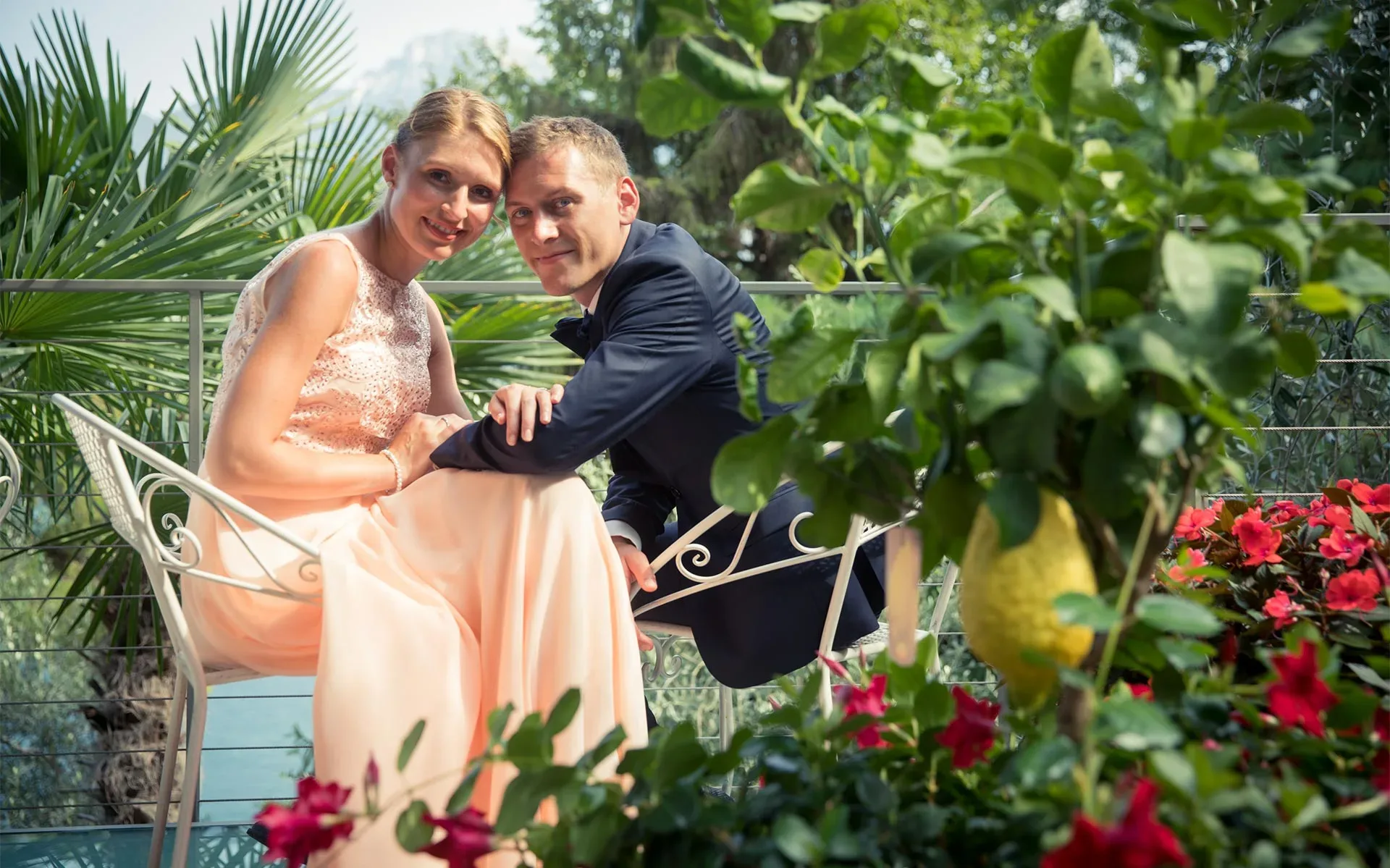 Coppia elegante seduta in giardino tra piante tropicali e fiori