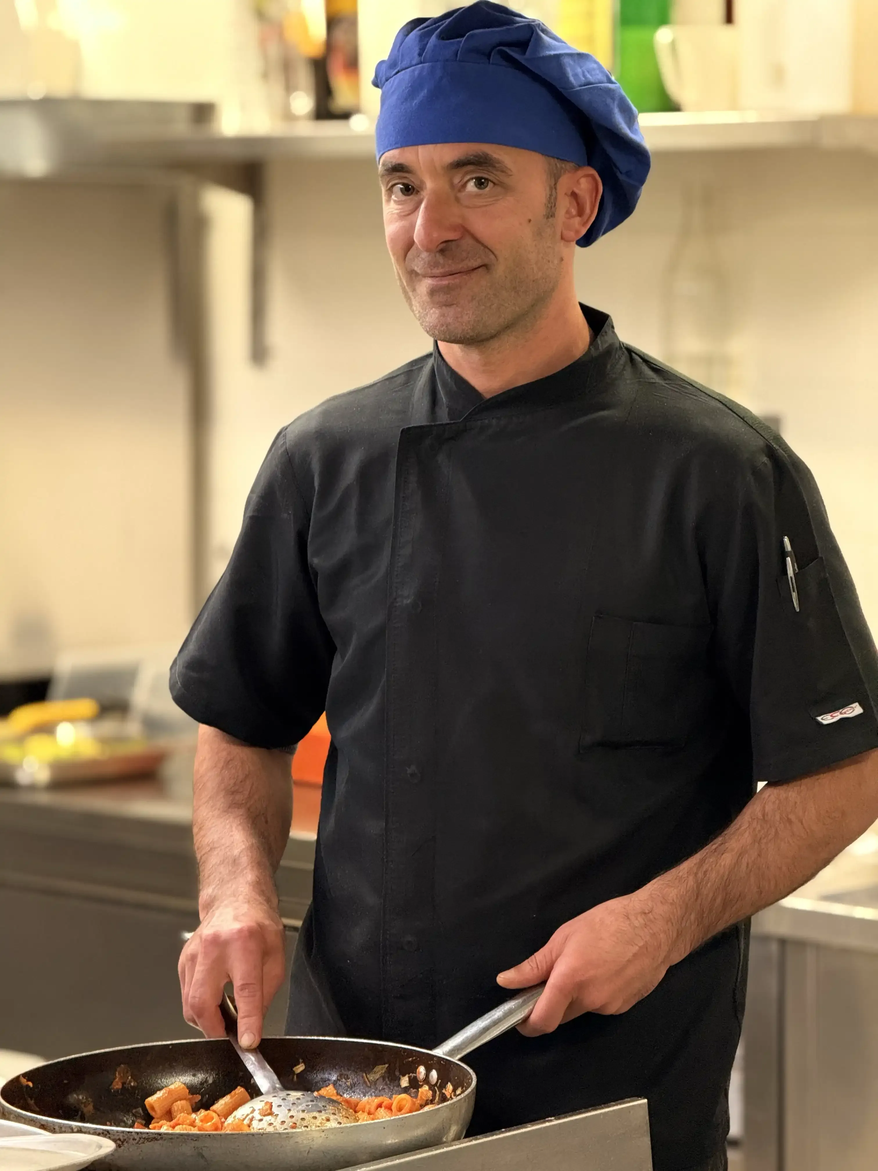 Cuoco con cappello blu cucina pasta in padella