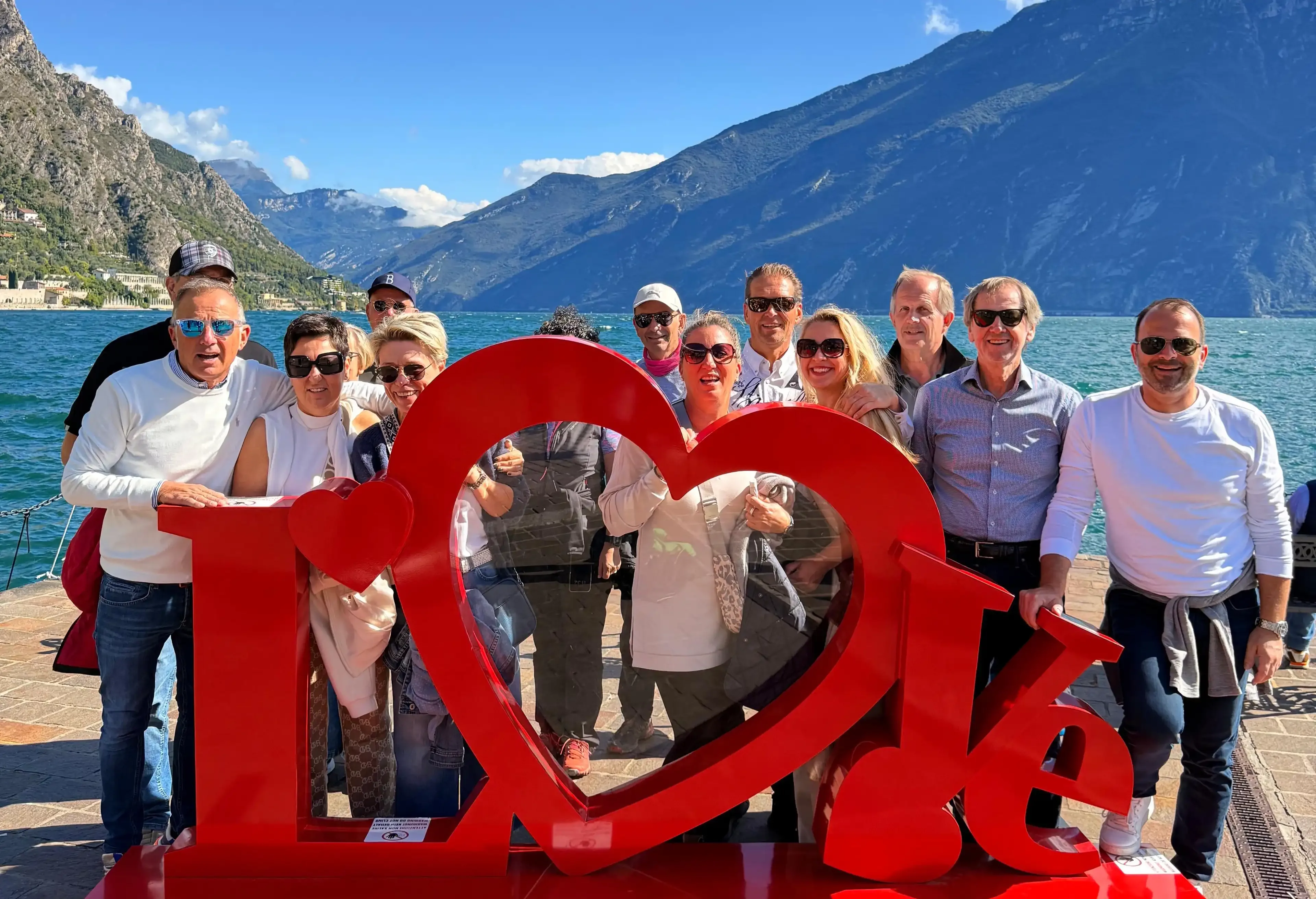 Gruppo di turisti davanti a una scultura rossa con cuore, sul lago tra le montagne