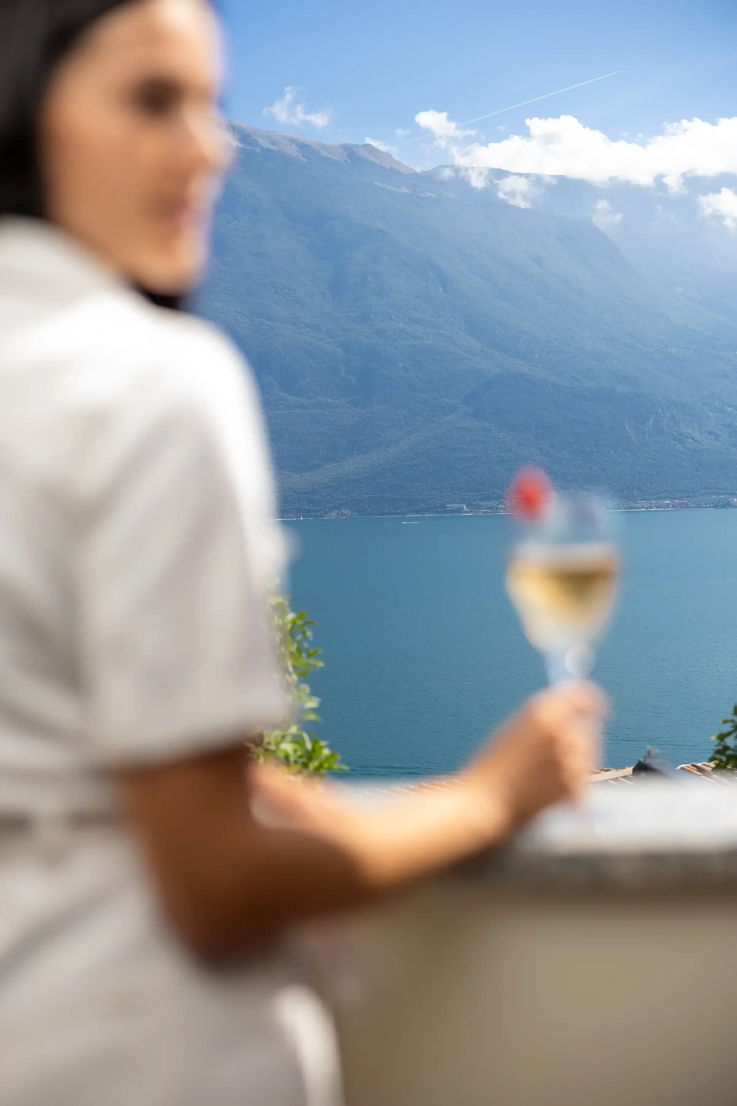 Donna con bicchiere di vino osserva lago e montagne